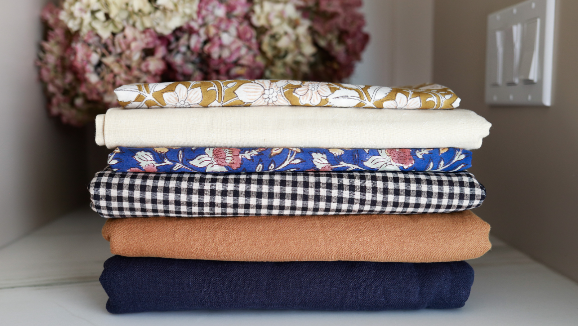 A stack of folded fabrics from small businesses is folded on a table.