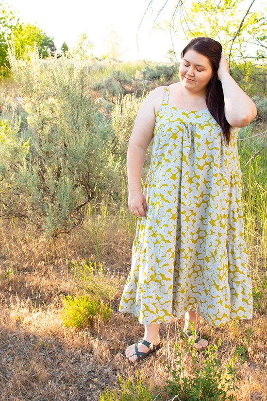 Woman stands amid greenery wearing a chartreuse midi length tiered Marcel Dress