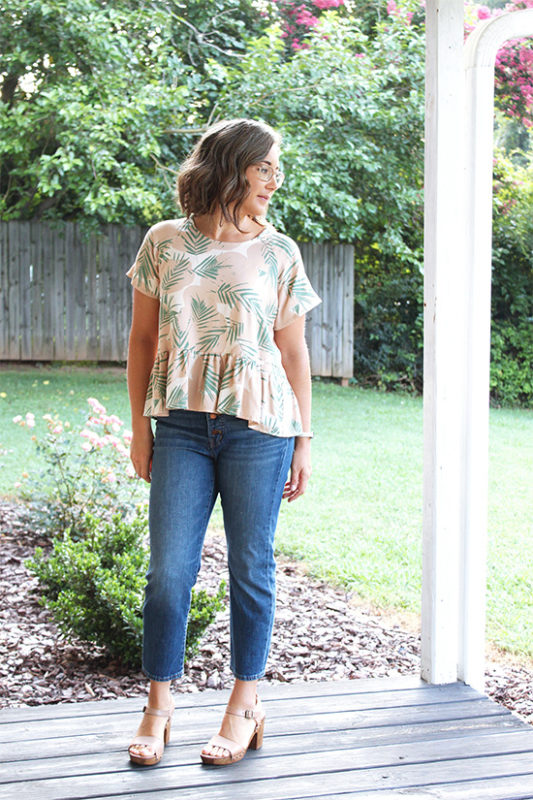 Woman wearing jeans and a Waterfall Raglan top stands in front of greenery. 