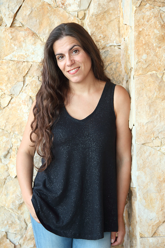 Woman wearing black v-neck Pony Tank Top stands in front of stone wall. 