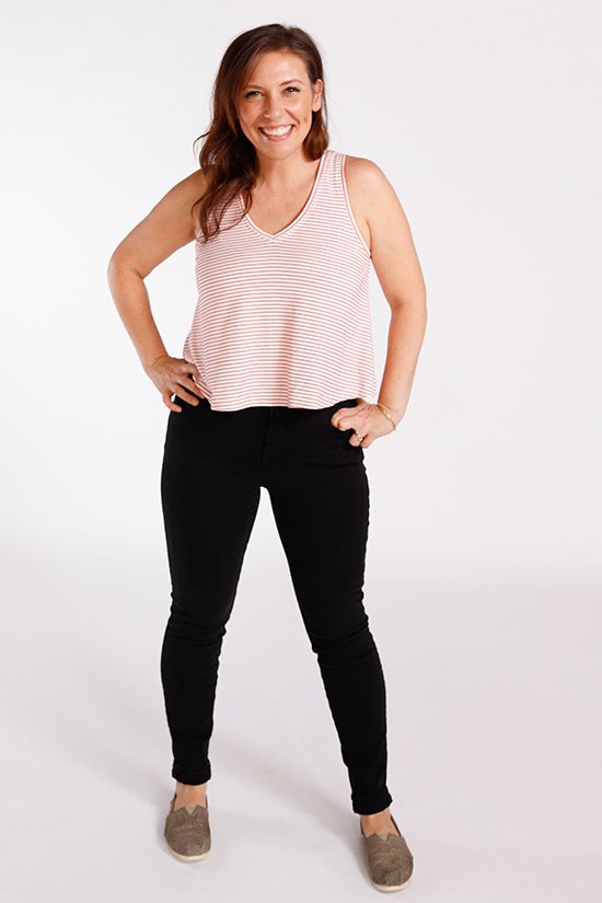 Woman wearing a cropped v-neck tank top stands in front of a white background. 