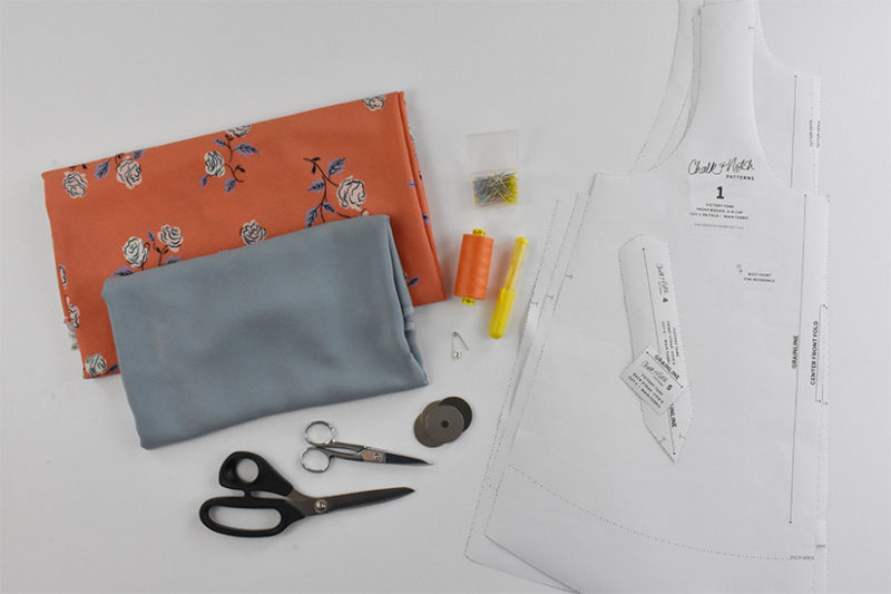 Fabric, scissors, pins, marking tools, pattern weights, and paper pattern pieces are laid on a white background.