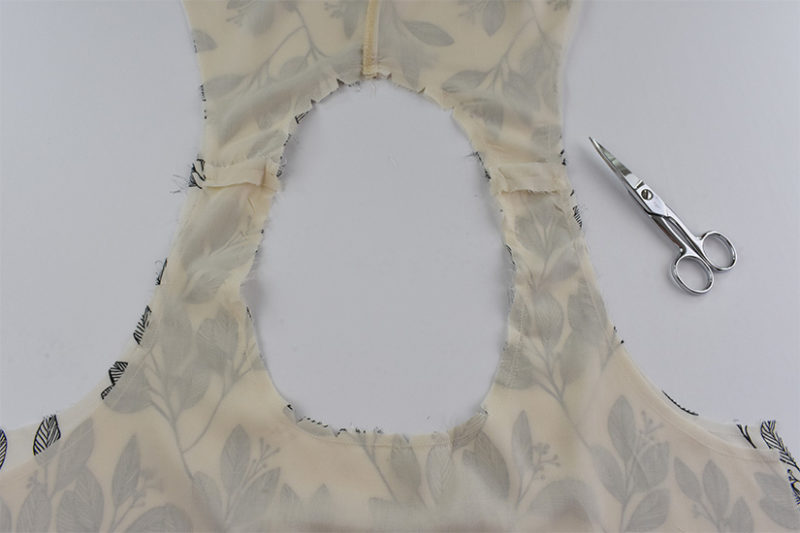 The wrong side of the fabric is shown at the neckline. Thread snips are visible to the right. 