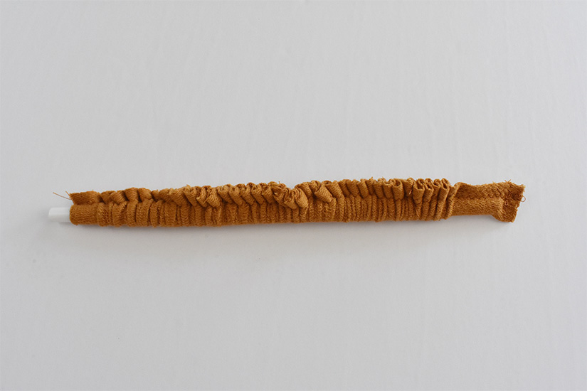 A yellow knit fabric tube is gathered onto a straw.