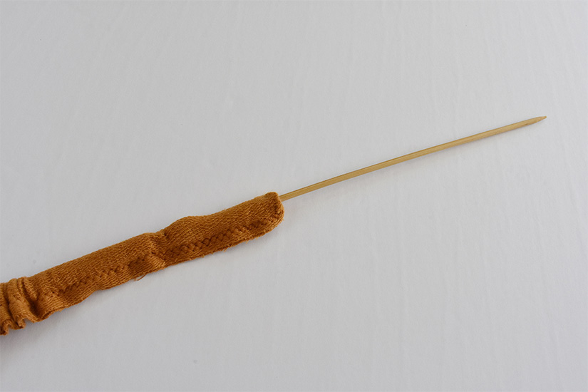 A wooden skewer is inserted into a yellow knit fabric tube.