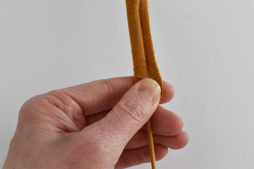 A hand holds a sewn yellow fabric tube. A wooden skewer is inserted into the tube. 