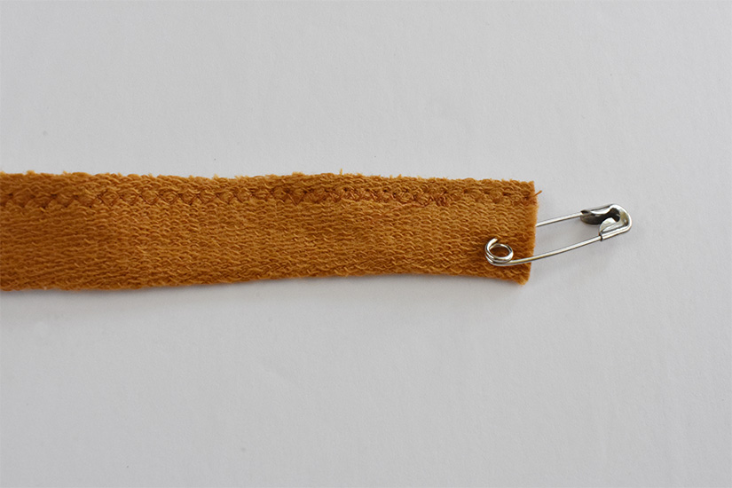 A safety pin is attached to the end of a yellow knit fabric tube.