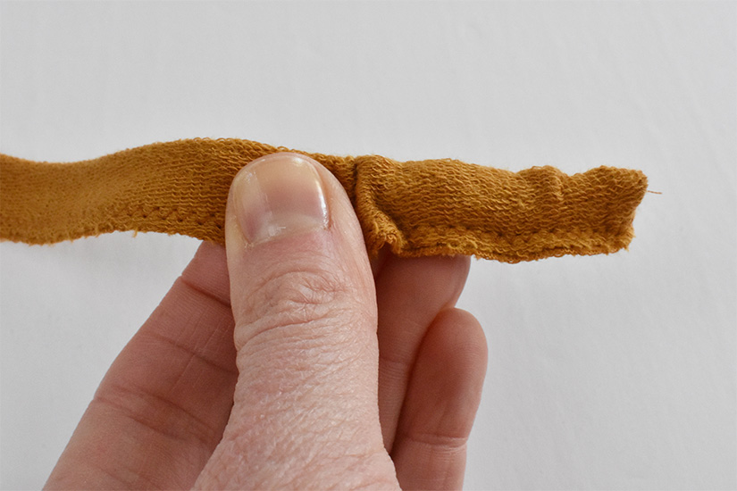 A hand holds a tube of knit fabric as it's turned right side out. 