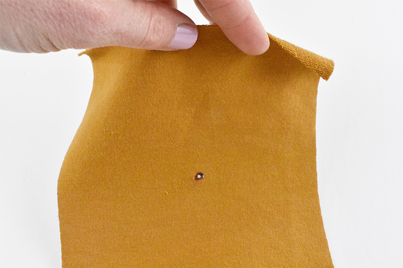 A small hole is shown at the marking on a yellow knit fabric