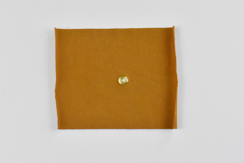 A brass grommet is shown installed in yellow knit fabric.
