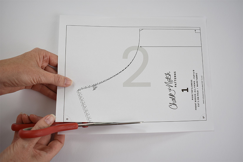 A person uses red scissors to cut along the border of a pdf sewing pattern page.