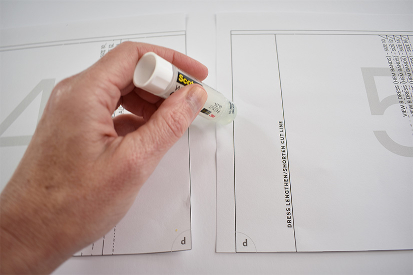 A person holding a glue stick applies glue to the edge of a pdf sewing pattern page