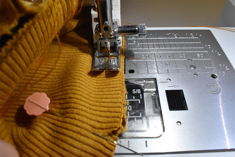 A sewing machine foot stitches on a yellow rib knit fabric. 