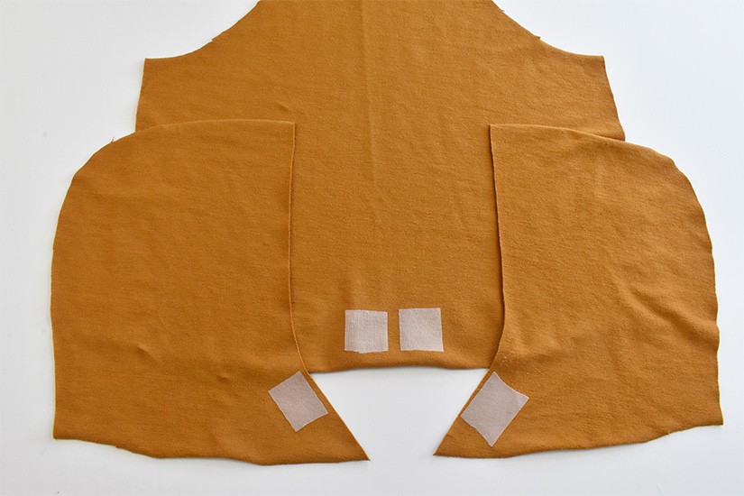 Small squares of fusible interfacing are shown fused to gold colored fabric pieces for the front bodice and hood of the Page Hoodie