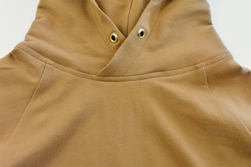 A close up of the topstitching on the neckline of a gold colored hoodie