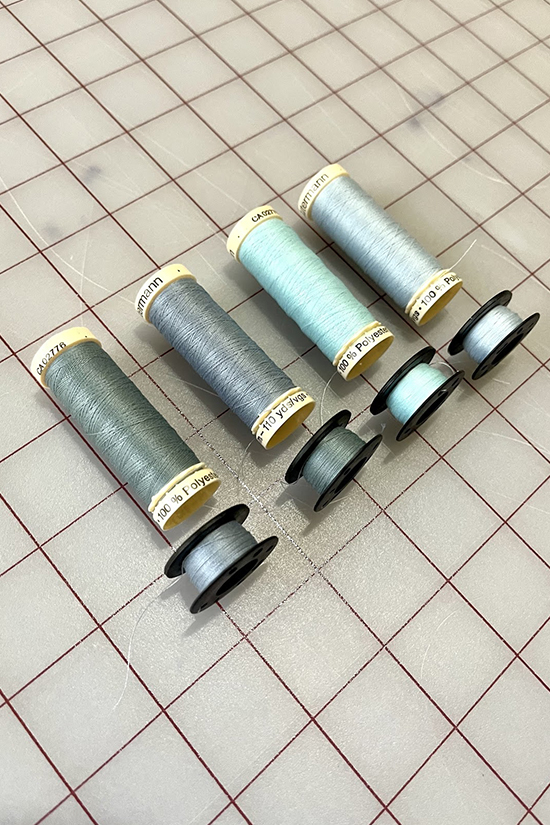 Four different colors of blue thread and bobbins laid on a cutting mat. 