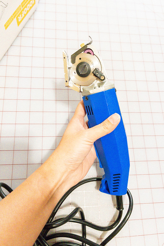 A hand holds an electric rotary cutter.