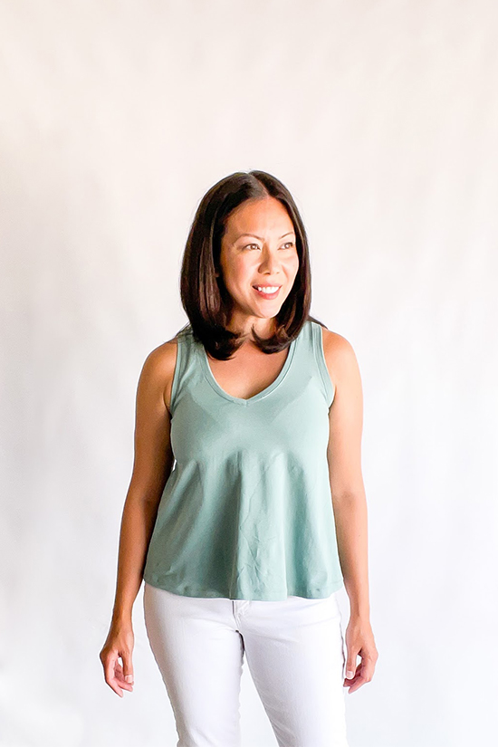 Michele wears a light blue/green tank top and stands in front of a white background.