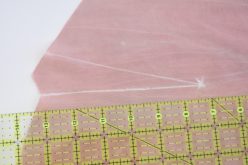 A dart is shown on pink fabric marked by white chalk.