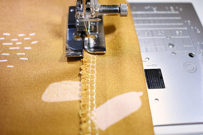 Yellow fabric is shown being sewn on a sewing machine. 