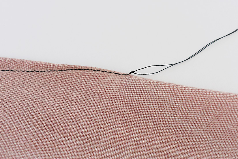A dart stitched with black thread and knotted at the end is shown on pink fabric.