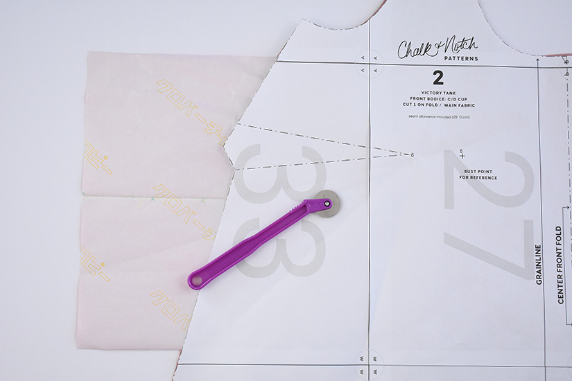 A paper sewing pattern, tracing paper and a tracing wheel are shown on white background. 