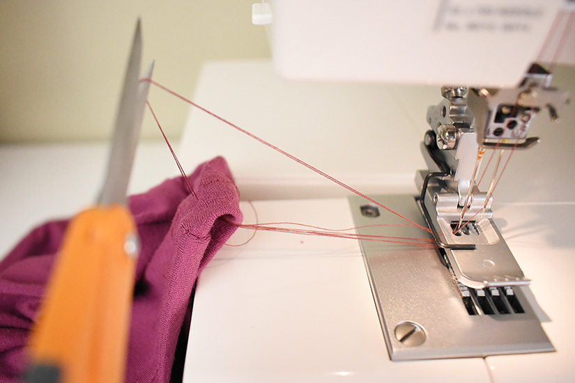 Scissors trim the threads of a coverstitch sewn hem.