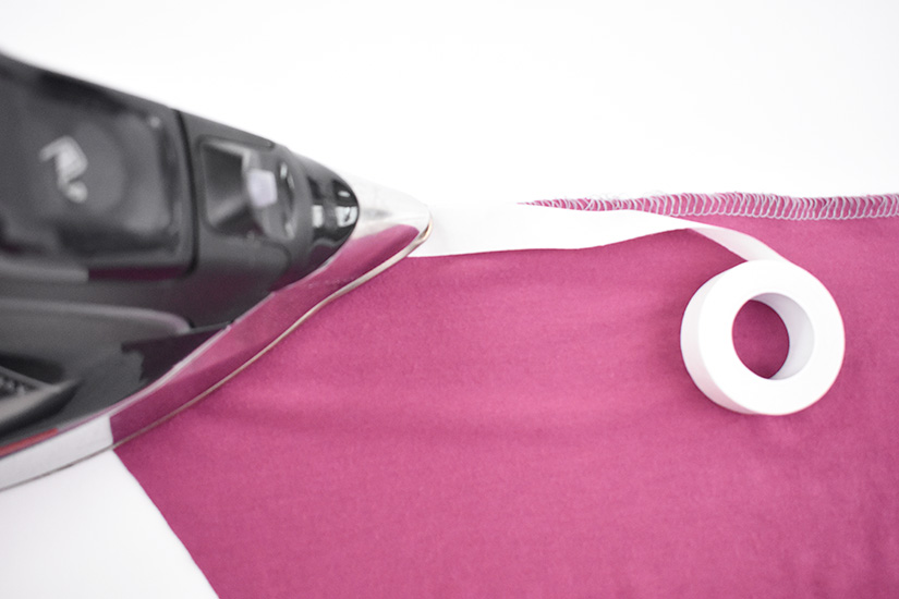 An iron presses a roll of heat n bond to the bottom of a hem.