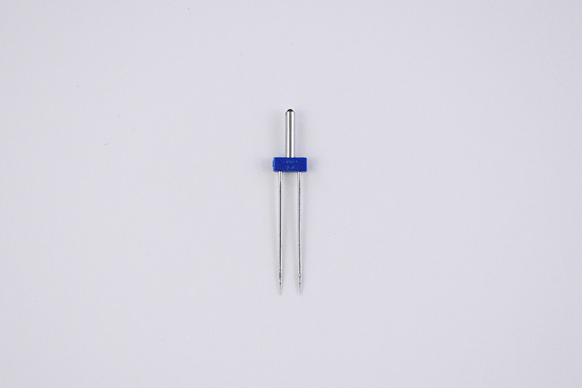 A double sewing needle lays on a white background.