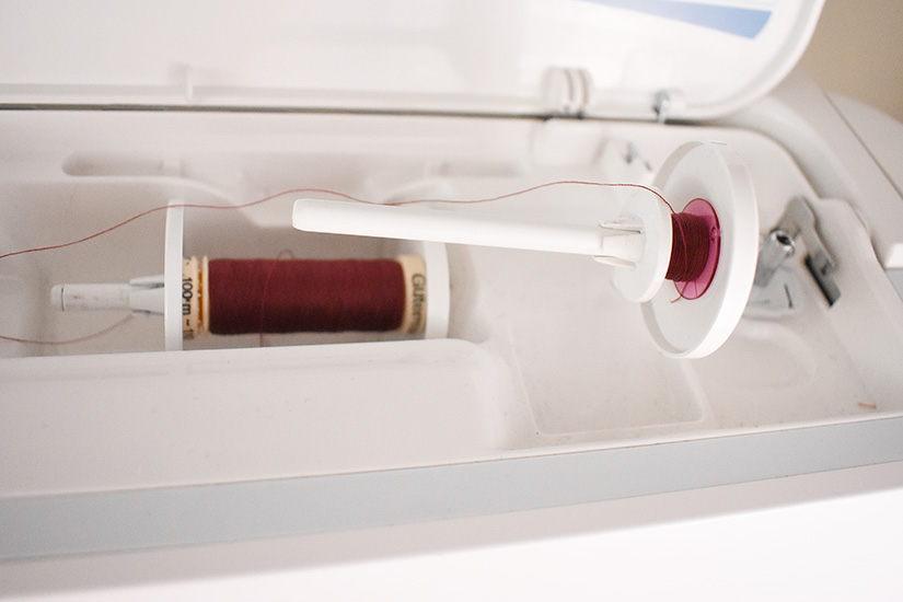 A sewing machine is threaded with a spool and bobbin of red thread.