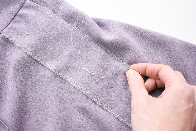 A hand stitches along the bottom of the Evelyn Skirt button placket