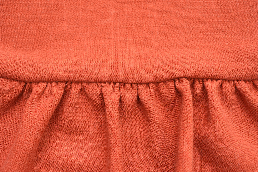 A close up of sewn gathers on orange fabric. 