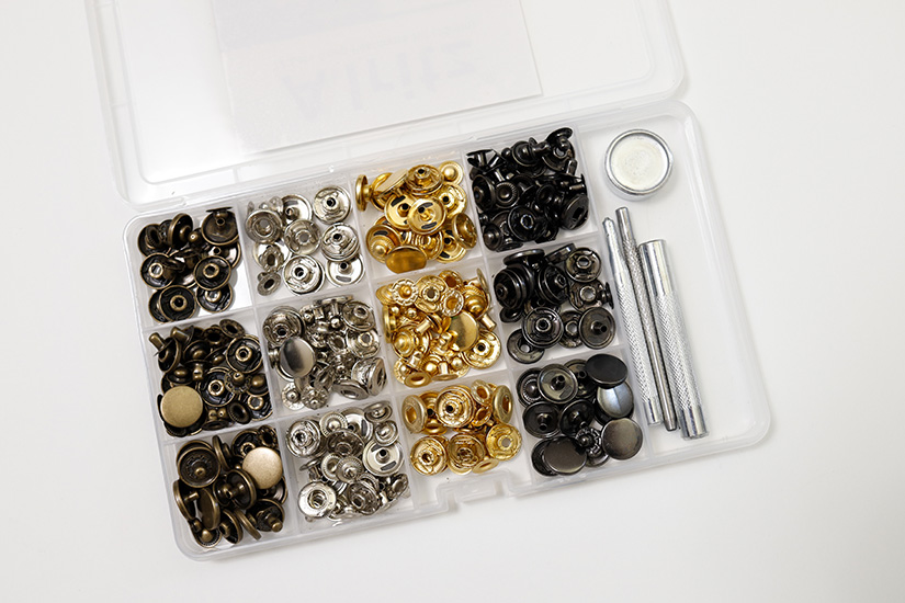 A plastic container showing metal snaps and setting supplies is shown on a white background. 