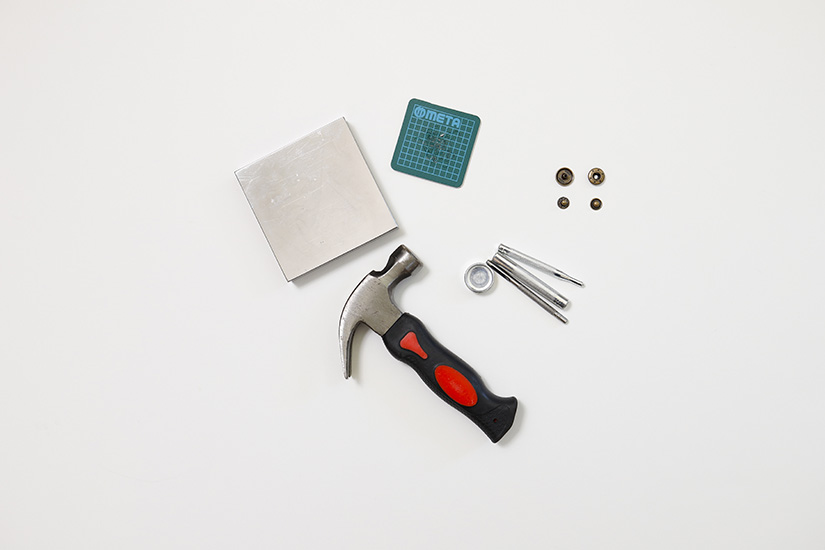 A hammer, snaps, and other snap setting supplies are shown on a white background. 