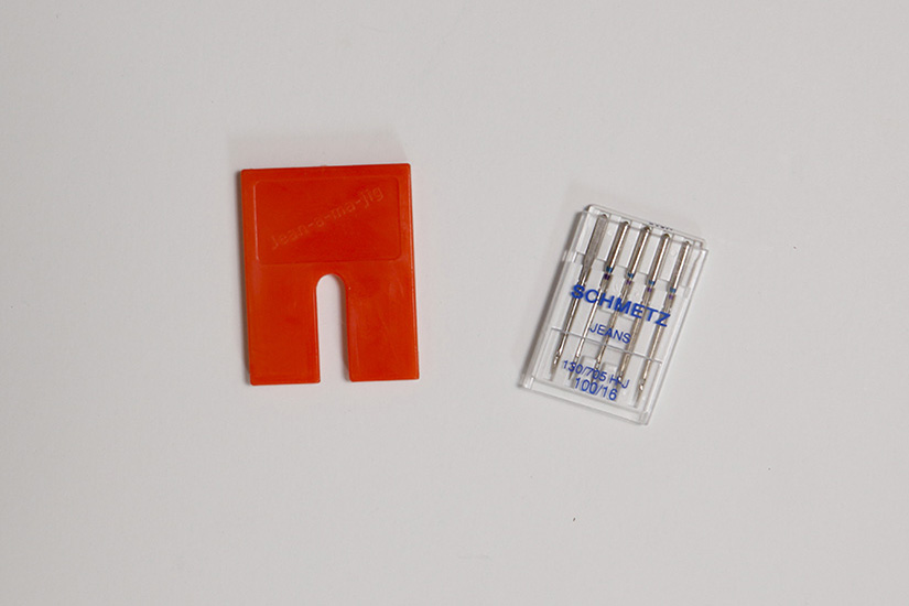 A bright orange seam jumper and a package of jeans sewing machine needles are shown on a white background. 