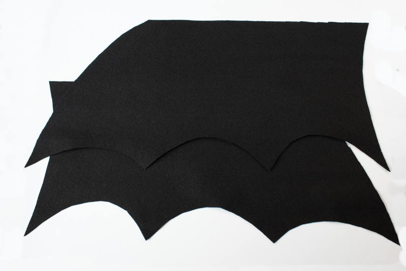 Two Halloween costume felt bat wing pieces lay on a white background. 