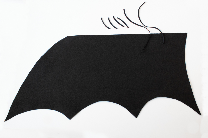 A felt bat wing and elastic pieces for a costume lay on a white background. 